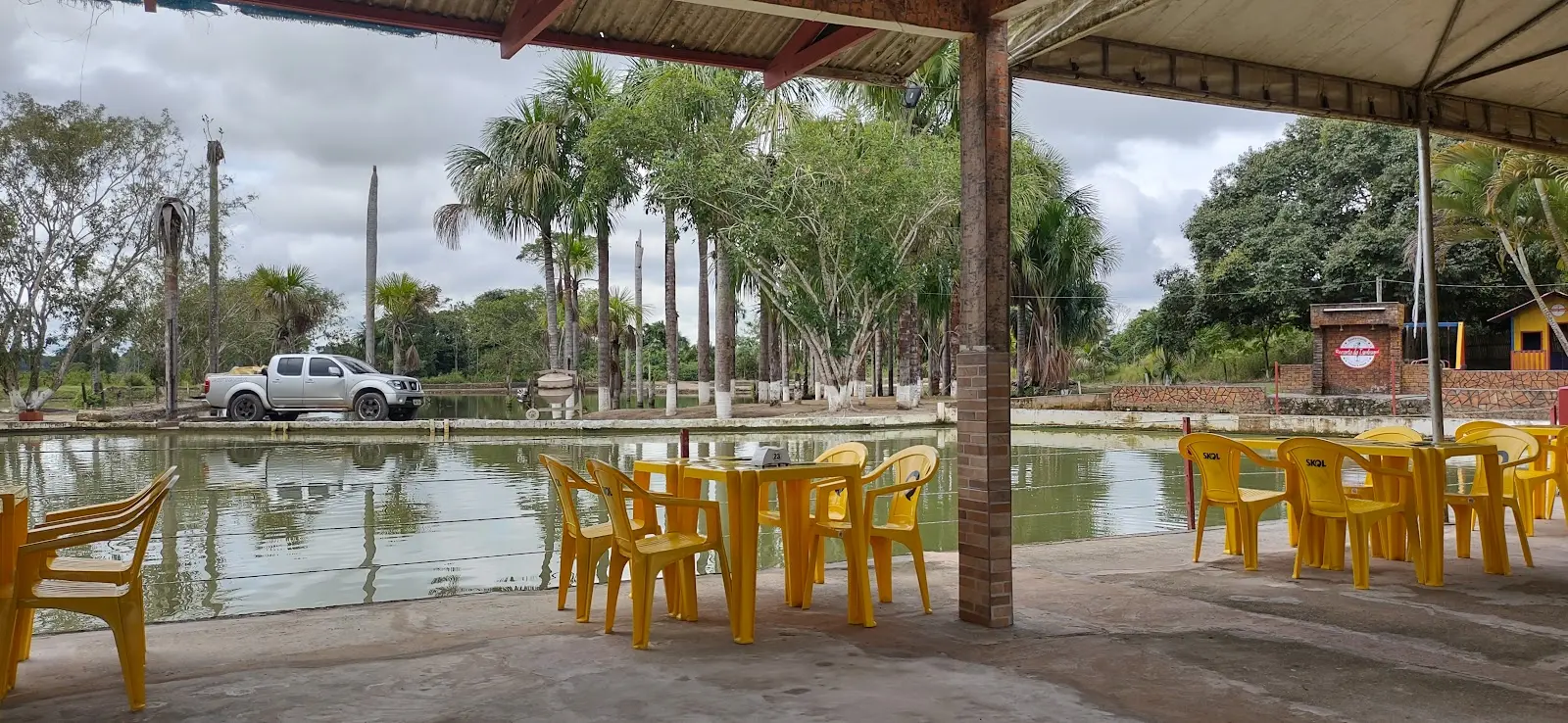 Área coberta com mesas amarelas à beira do lago do Recanto do Tambaqui, em Rio Branco