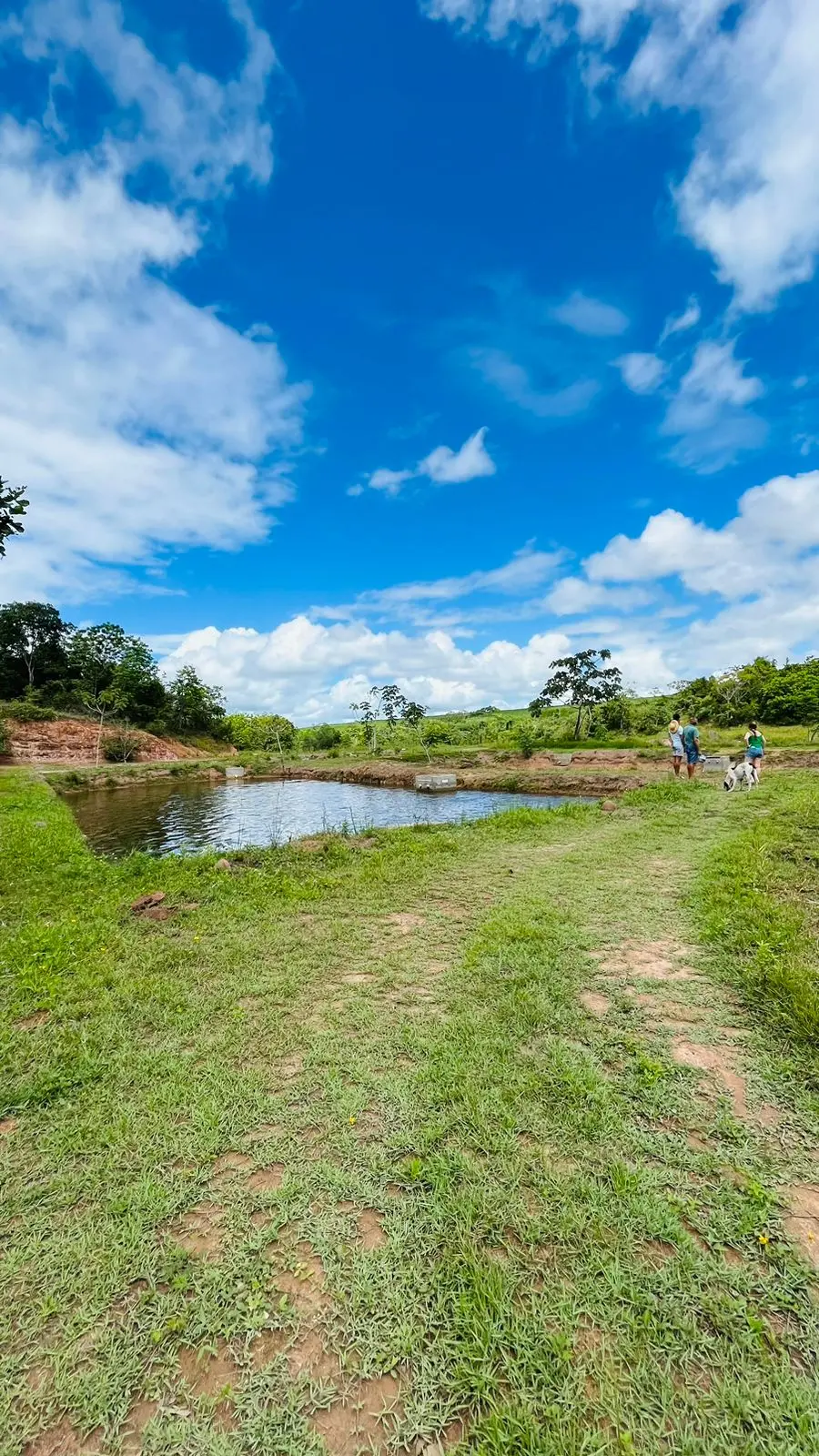 Tanque do Pesqueiro Sabiá cercado de gramado, com visitantes caminhando na margem