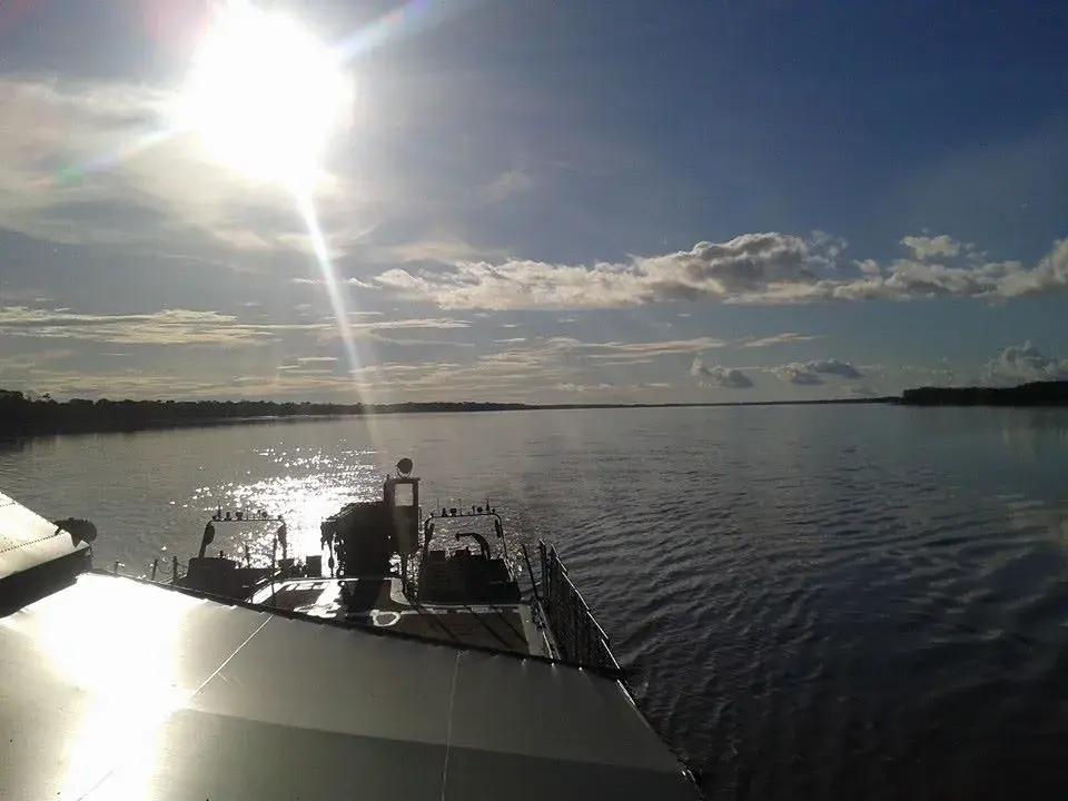 Barco de madeira navegando as águas barrentas do rio Solimões, com a mata fechada ao fundo