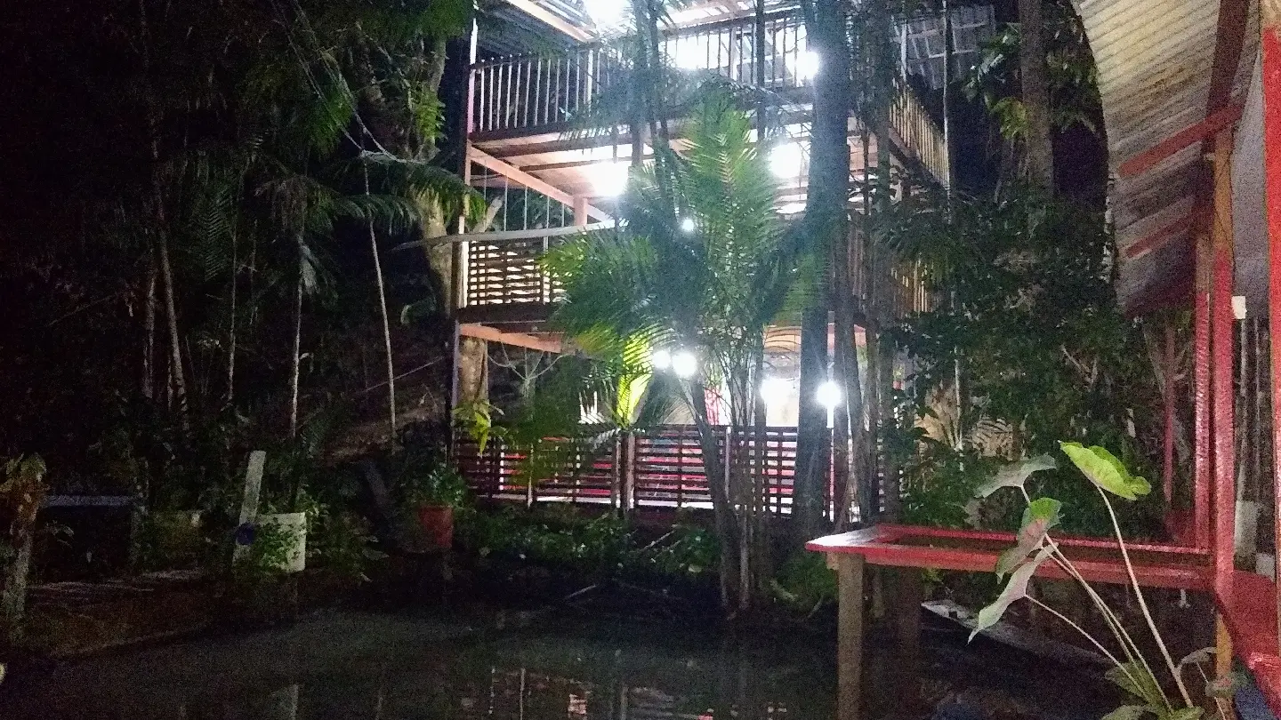 Construção de madeira do Pague Pesque Manaus iluminada à noite, cercada de plantas e com a água em primeiro plano