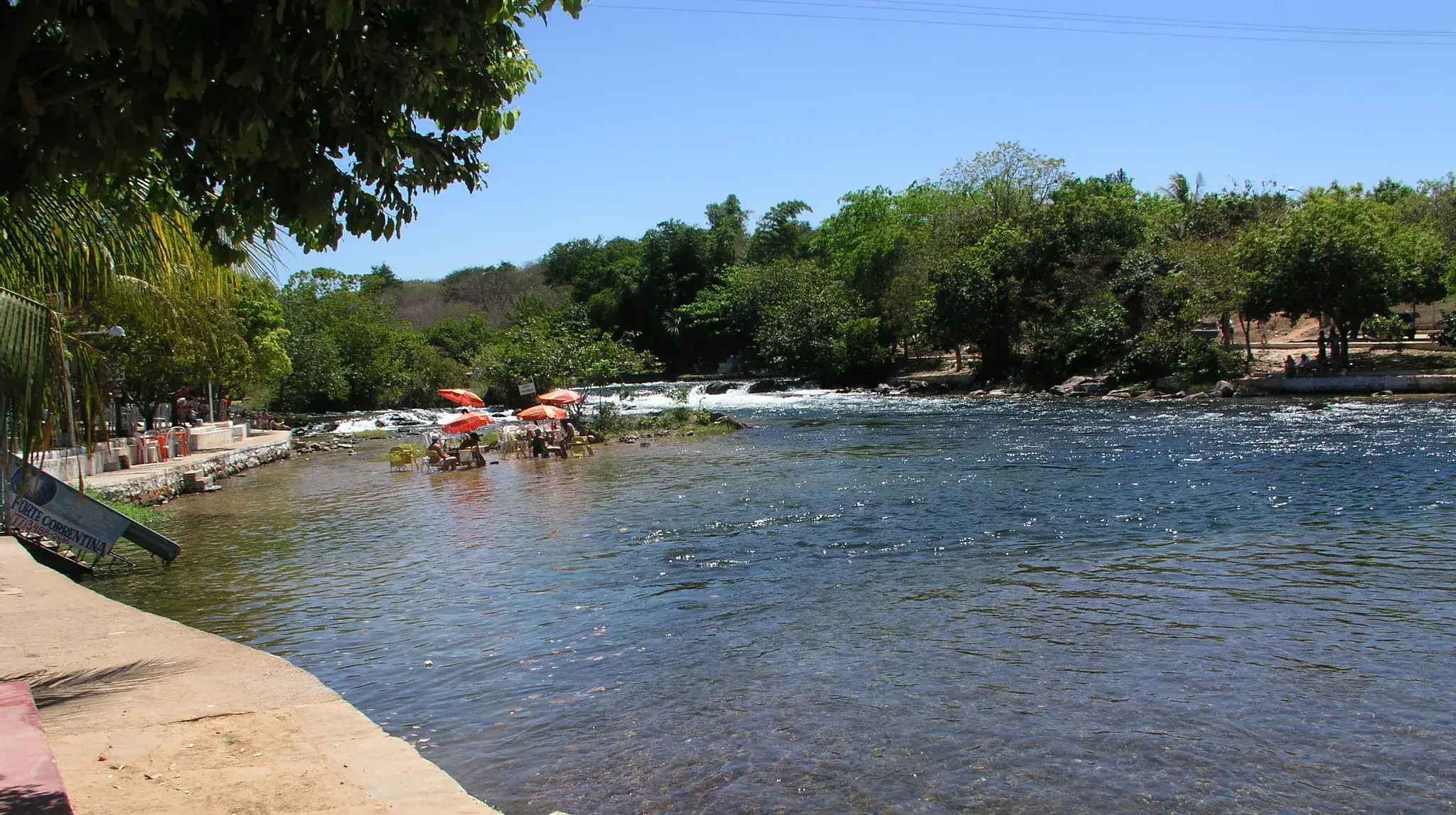 Rio das Éguas de água clara e correnteza rasa, com mata na margem e banhistas perto de uma pequena corredeira