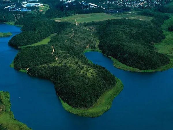 Margem arborizada da Lagoa do Juara, na Serra, com a água calma ao fundo