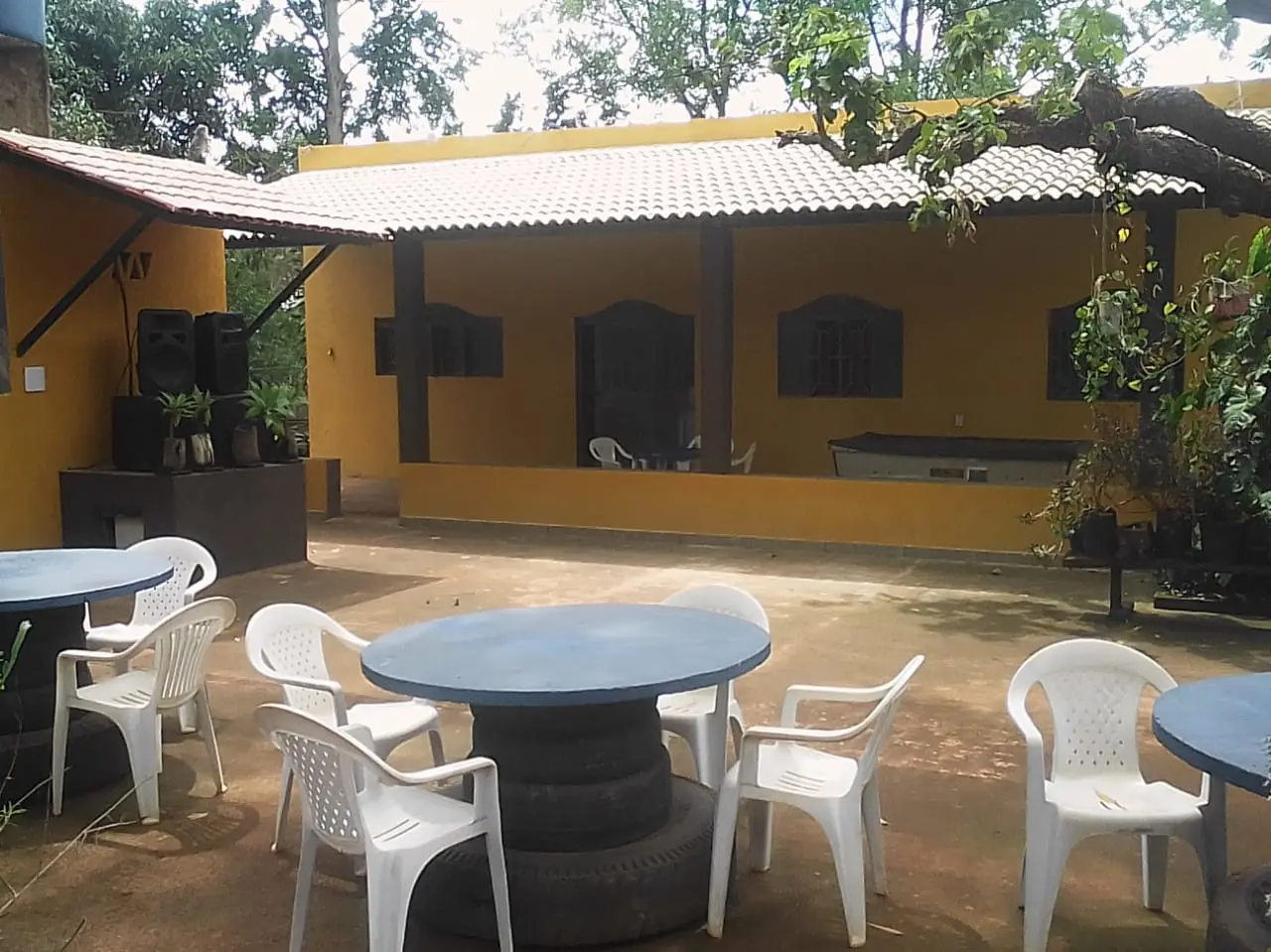 Pátio com mesas e cadeiras brancas diante da casa amarela do Noronha Pesque Pague