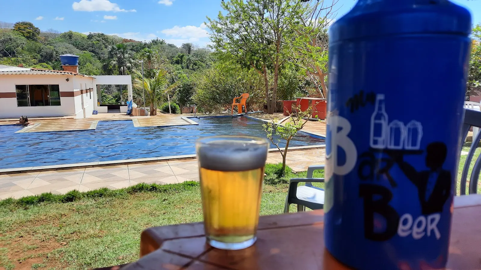 Piscina e casa de apoio do Pesque e Pague do Zé Mendes, com um copo de cerveja em primeiro plano