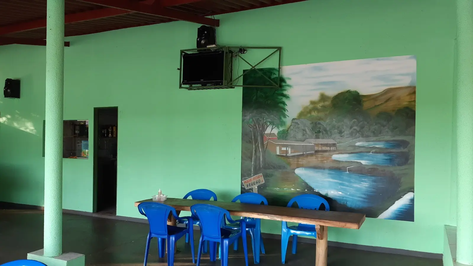 Salão do Pesque e Pague do Fedego com mesa comprida, cadeiras azuis e um mural pintado do lago