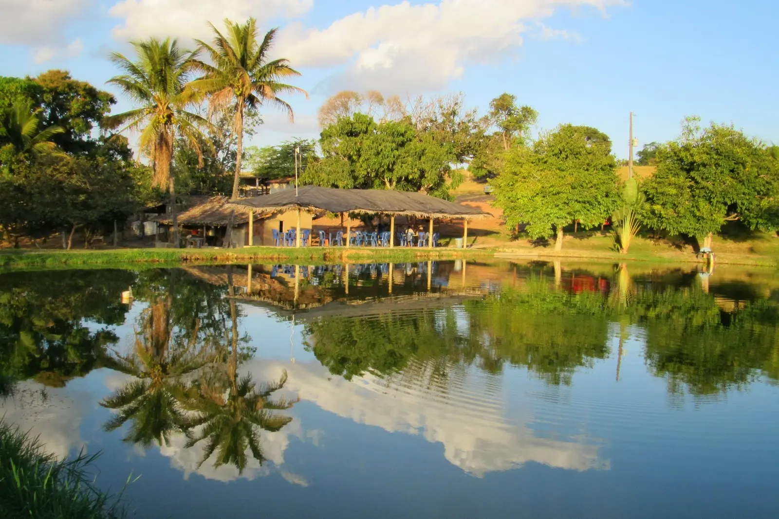 Lago do Pesque Pague Baunilha com o quiosque de palha e as mesas azuis na margem