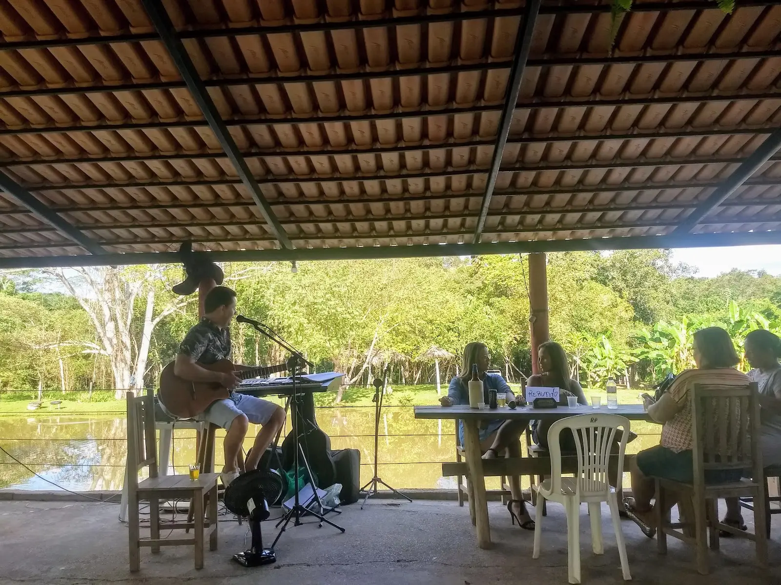 Músico tocando na varanda coberta do Pesque Pague Recanto dos Amigos, com o lago ao fundo