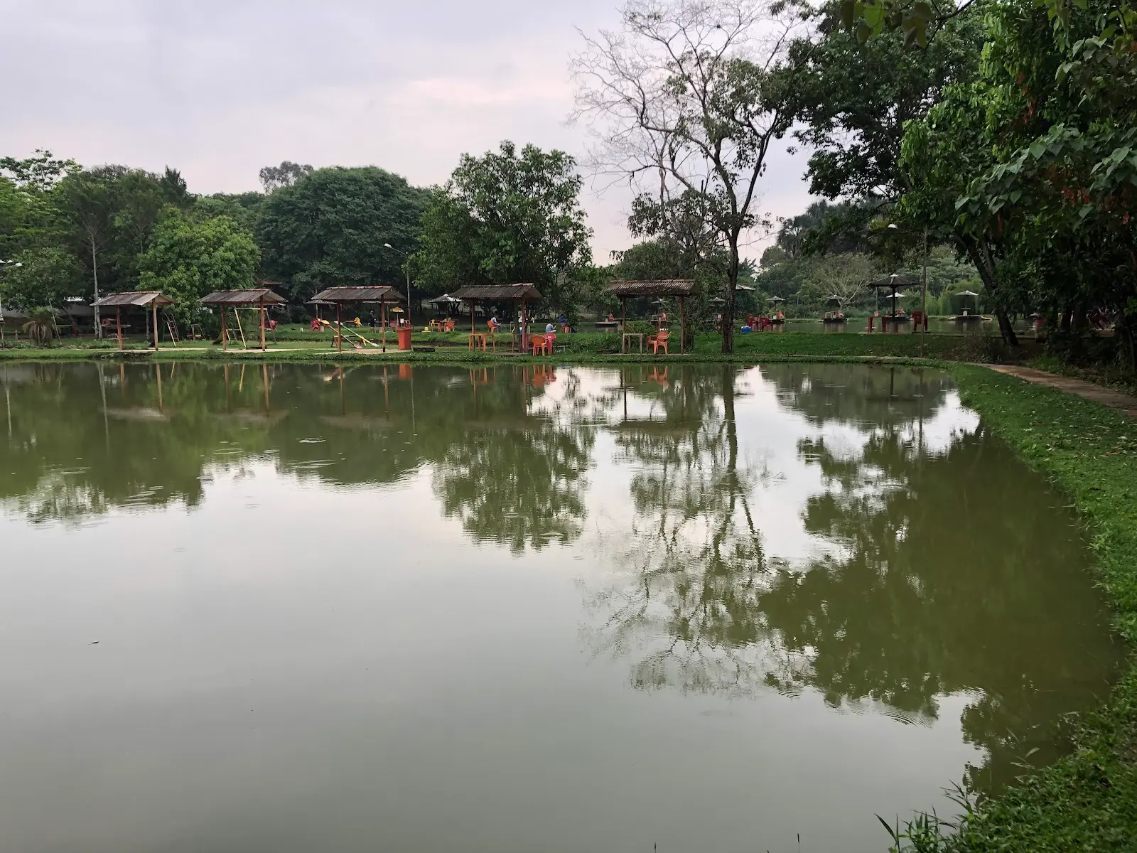Lago do Clube de Pesca Poço dos Pintados com quiosques de palha e mesas na margem oposta