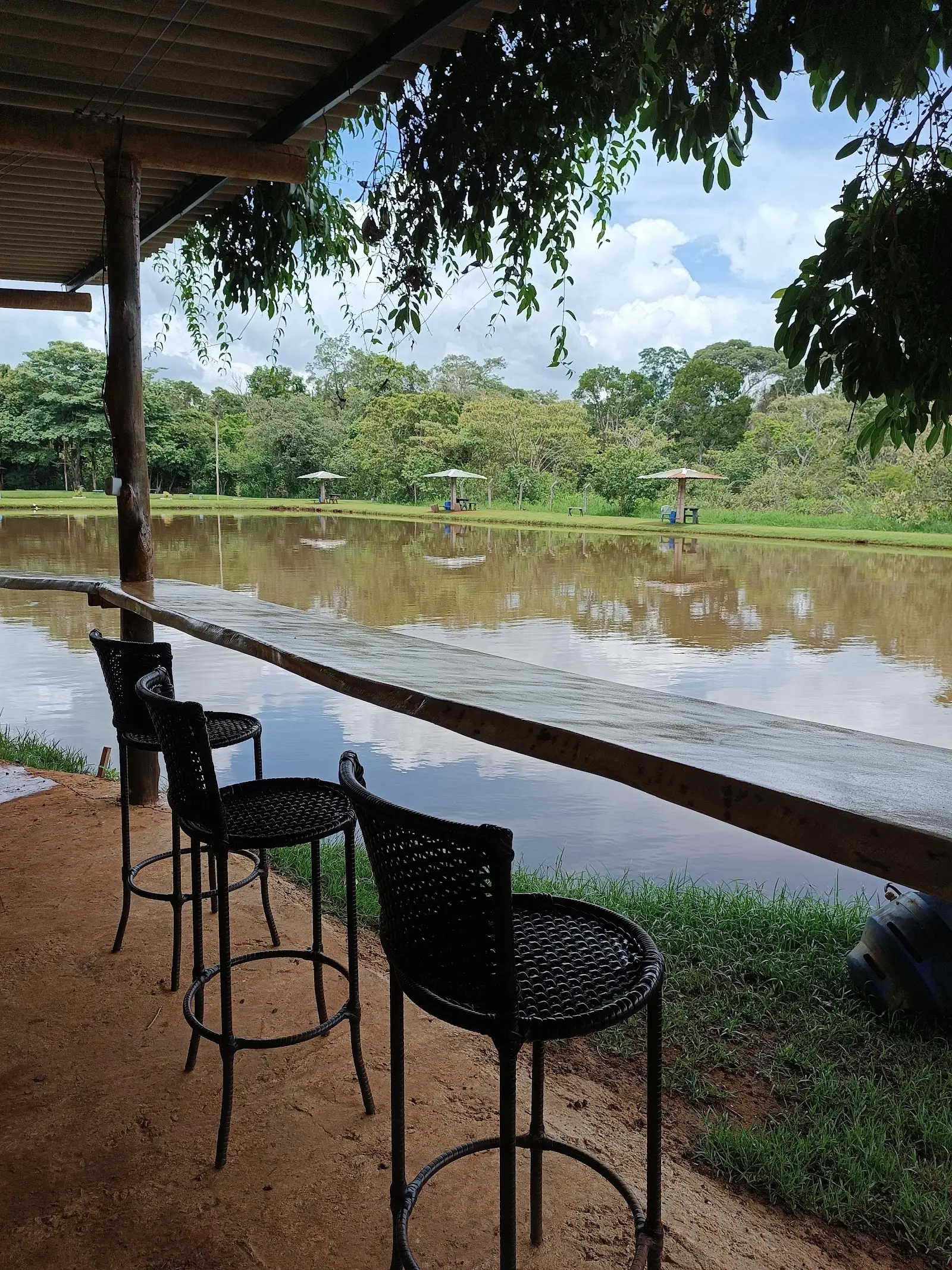 Balcão com banquetas de frente para o lago do Pesque e Pague do Temir, com quiosques na outra margem