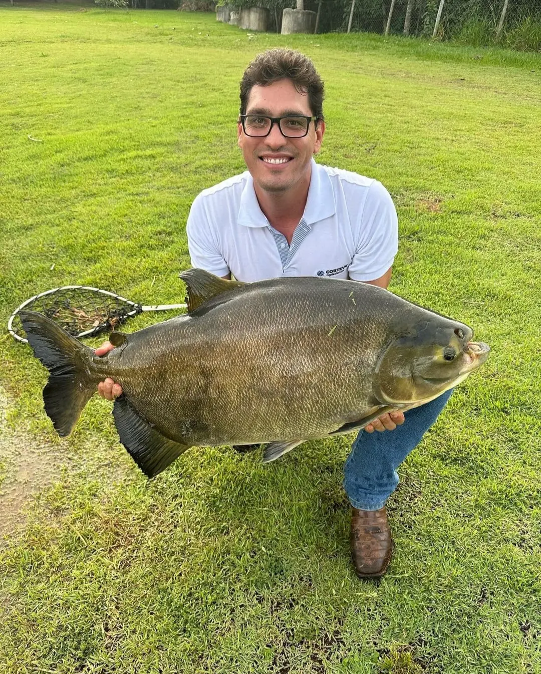 Pescador segurando um tambaqui grande num gramado, em foto publicada pelo Pesque Pague 2 Irmãos