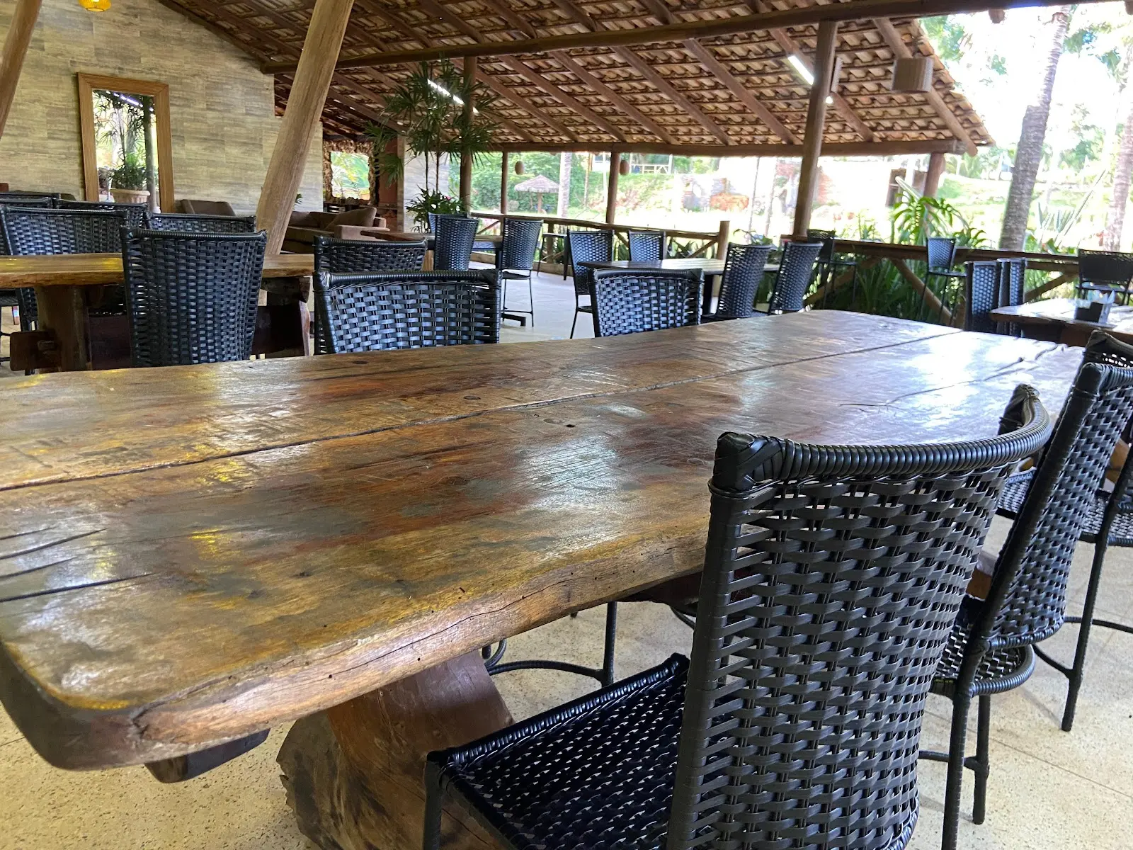 Mesa rústica de madeira e cadeiras de fibra no salão coberto do Pesque Pague Aldeias