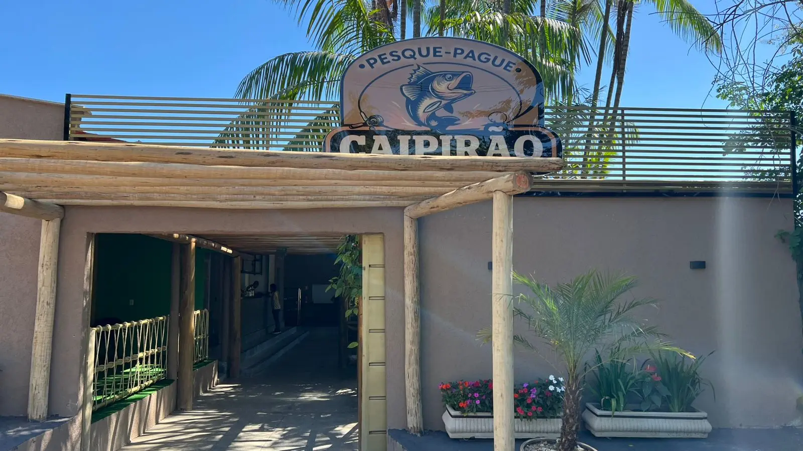 Entrada do Pesque Pague Caipirão, com a placa sobre um pergolado de madeira, em Trindade