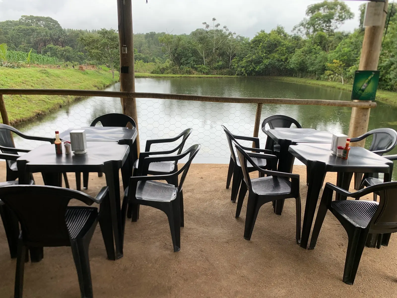 Mesas de um salão aberto de frente para o lago do Pesque-pague da Sandra, com mata ao fundo