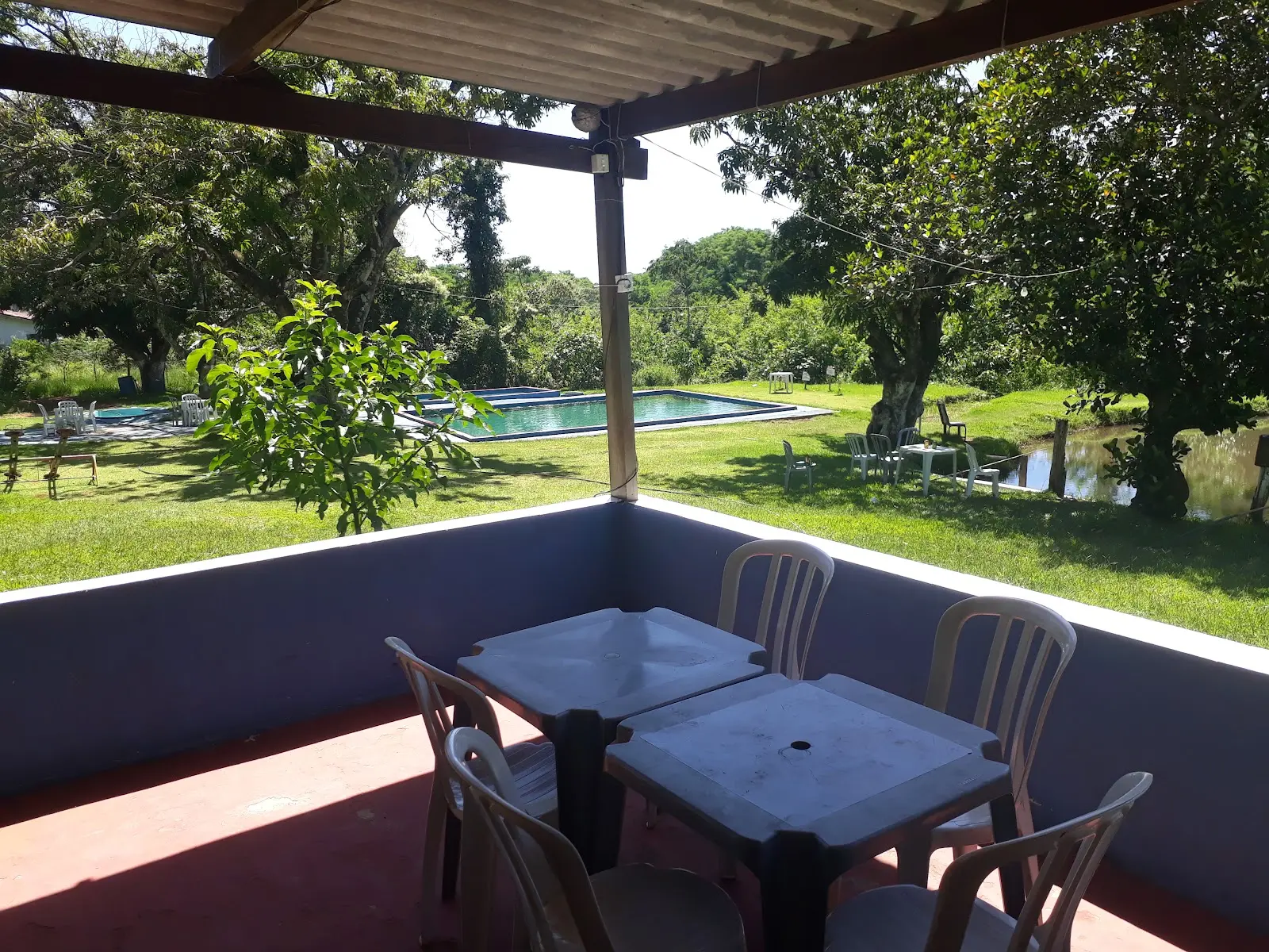 Varanda com mesas de frente para a piscina e o lago, cercados de gramado e árvores