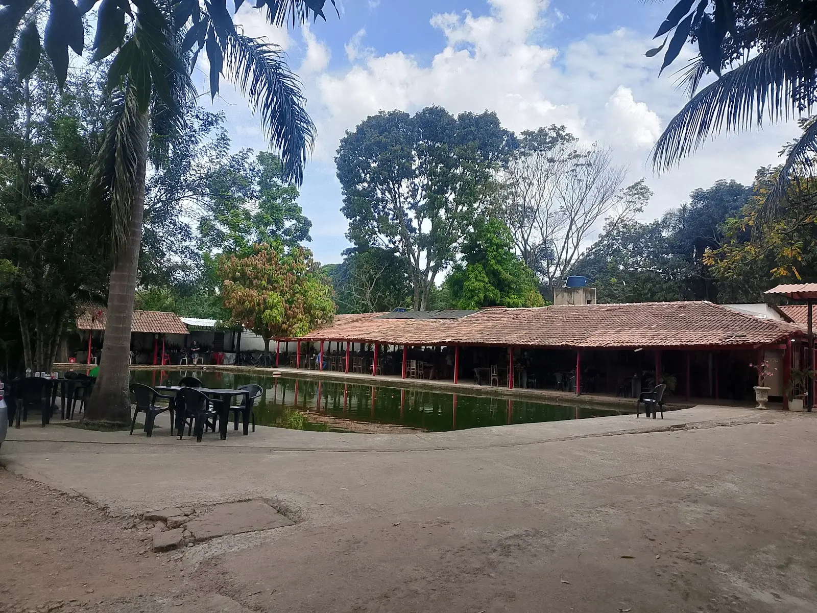 Tanque do Pesque Pague Pantanal com quiosques de telhado vermelho e palmeiras em volta
