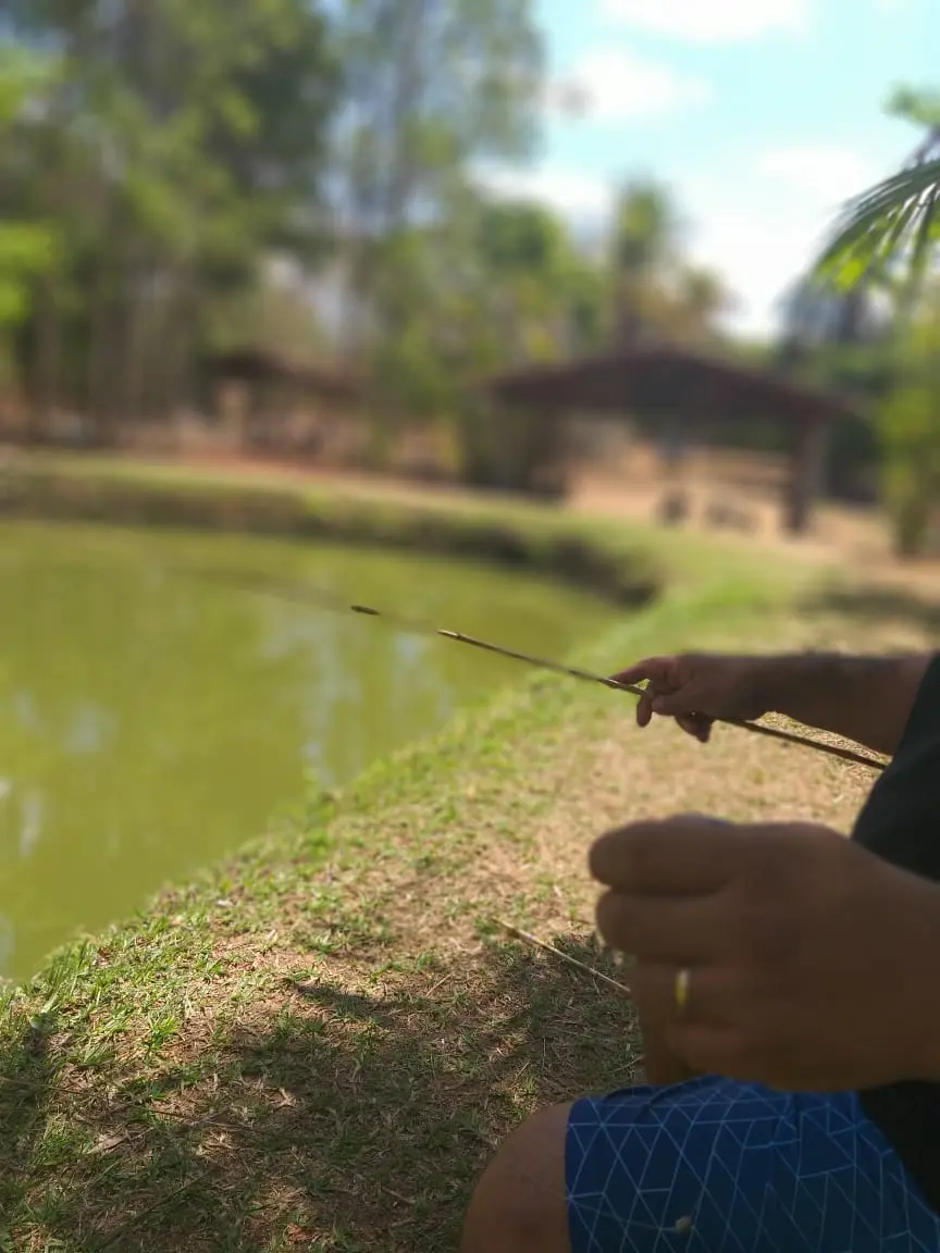 Pescador com vara de bambu na margem gramada do Pesqueiro do Bode, em Trindade