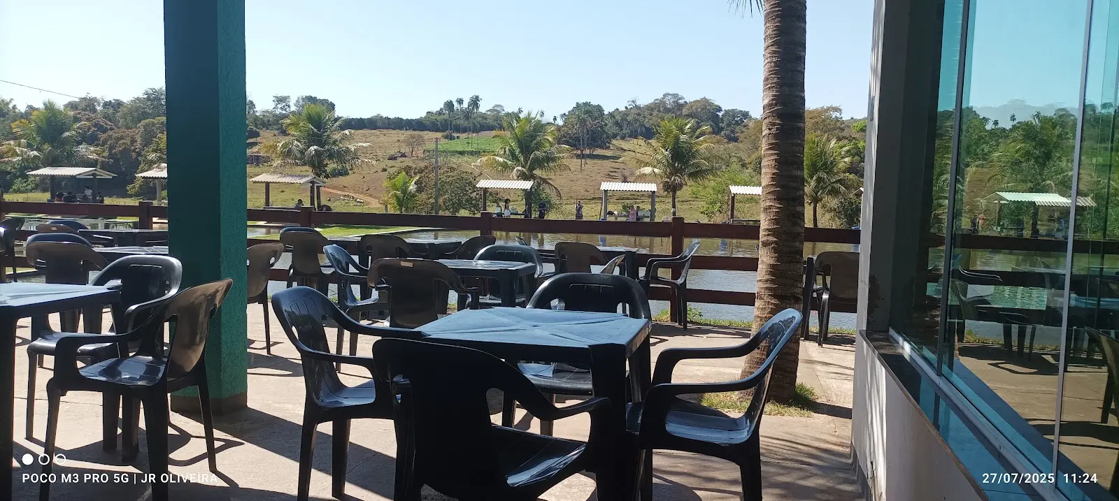 Mesas na varanda do Pesqueiro WR de frente para o lago, com quiosques na outra margem