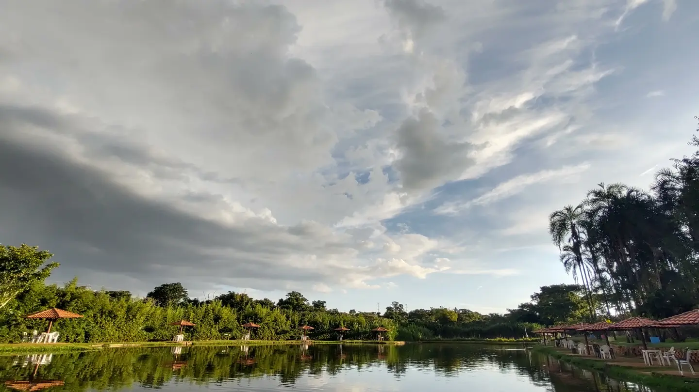 Lago do Recanto da Matrinxã com quiosques de telhado vermelho na margem e palmeiras sob céu nublado