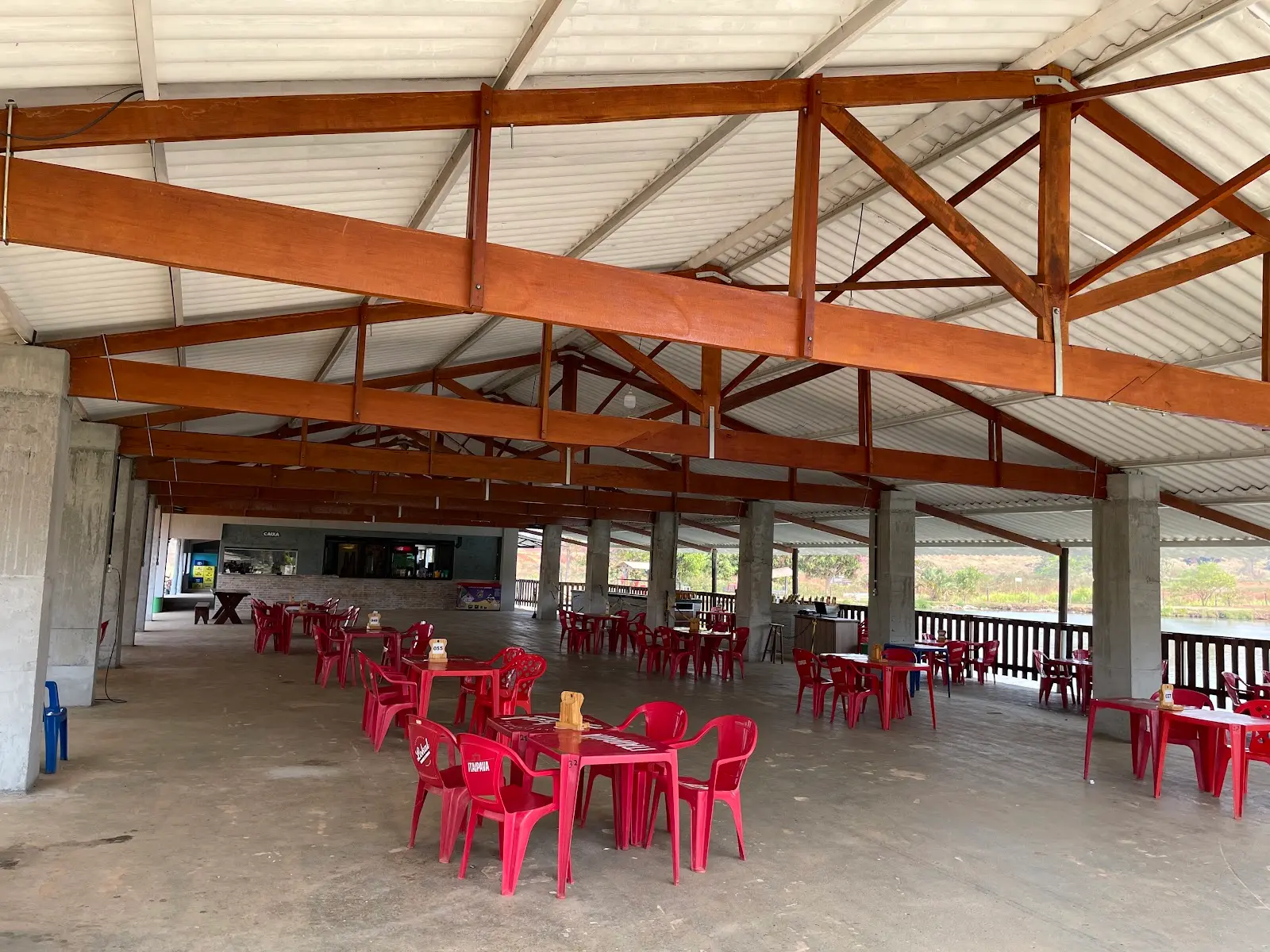 Salão coberto com mesas e cadeiras vermelhas e vista para a área externa