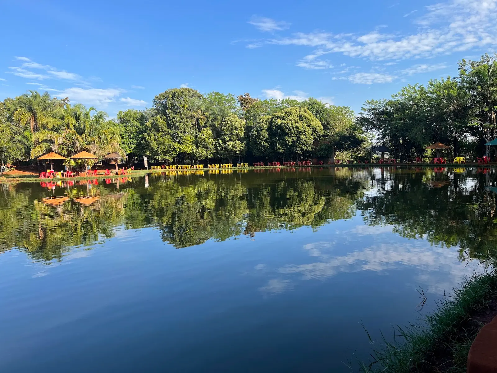 Lago do Clube de Pesca do André com quiosques de palha e mesas na margem