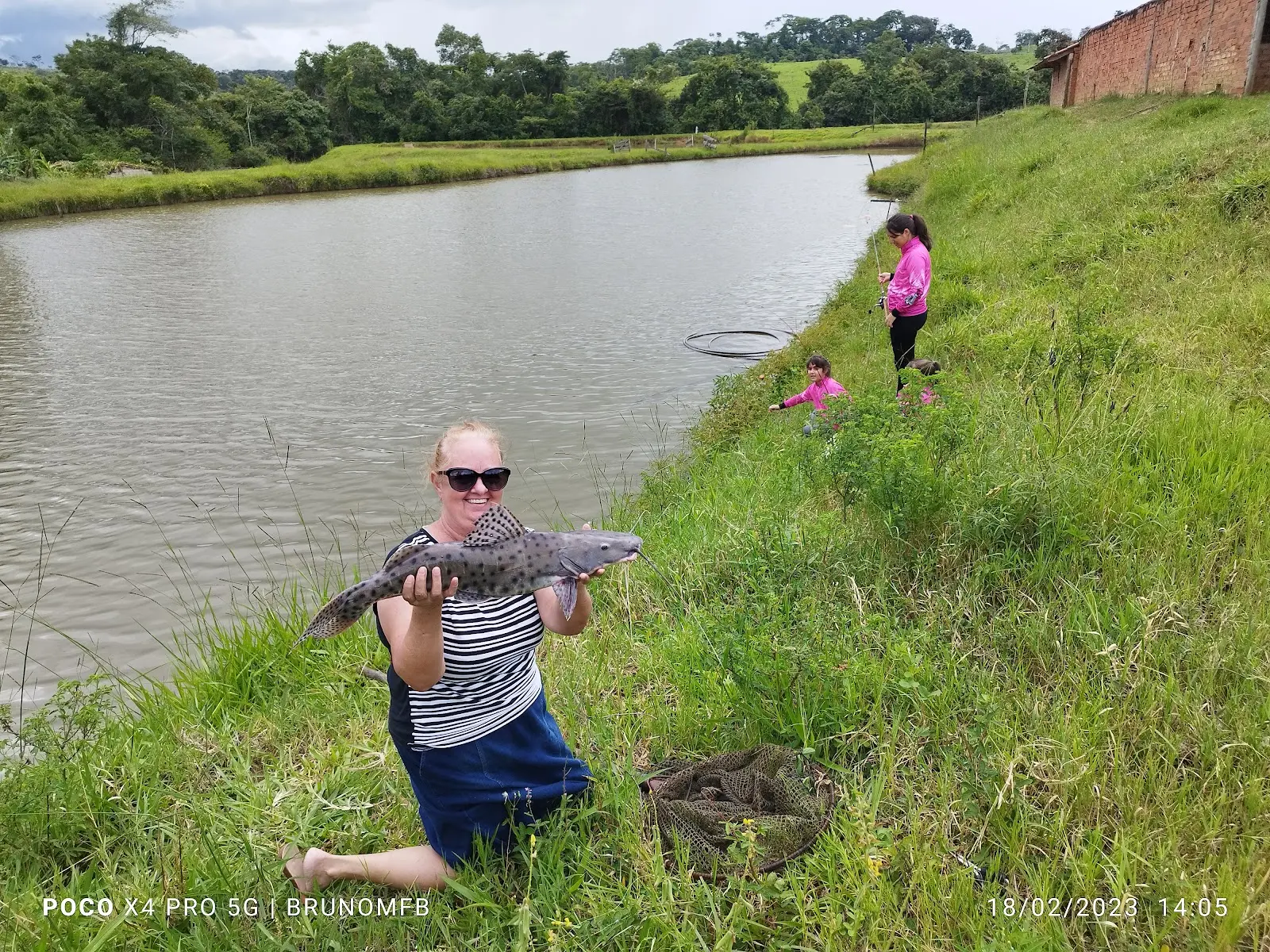 Pescadora segurando um pintado na margem de um poço do Pesque Pague Tocantins, com crianças pescando ao fundo