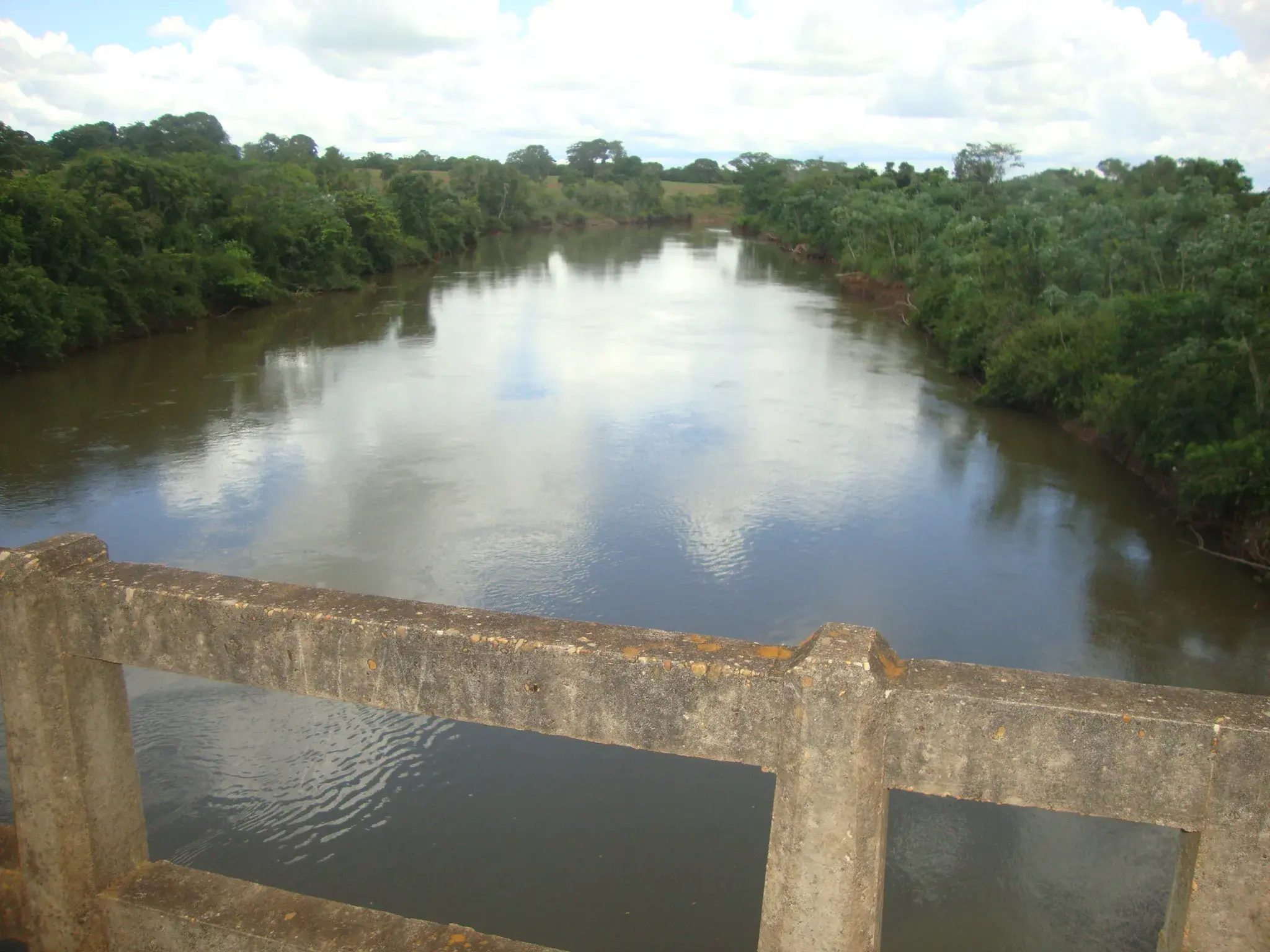 Rio Corrente visto de uma ponte de concreto, com mata nas margens