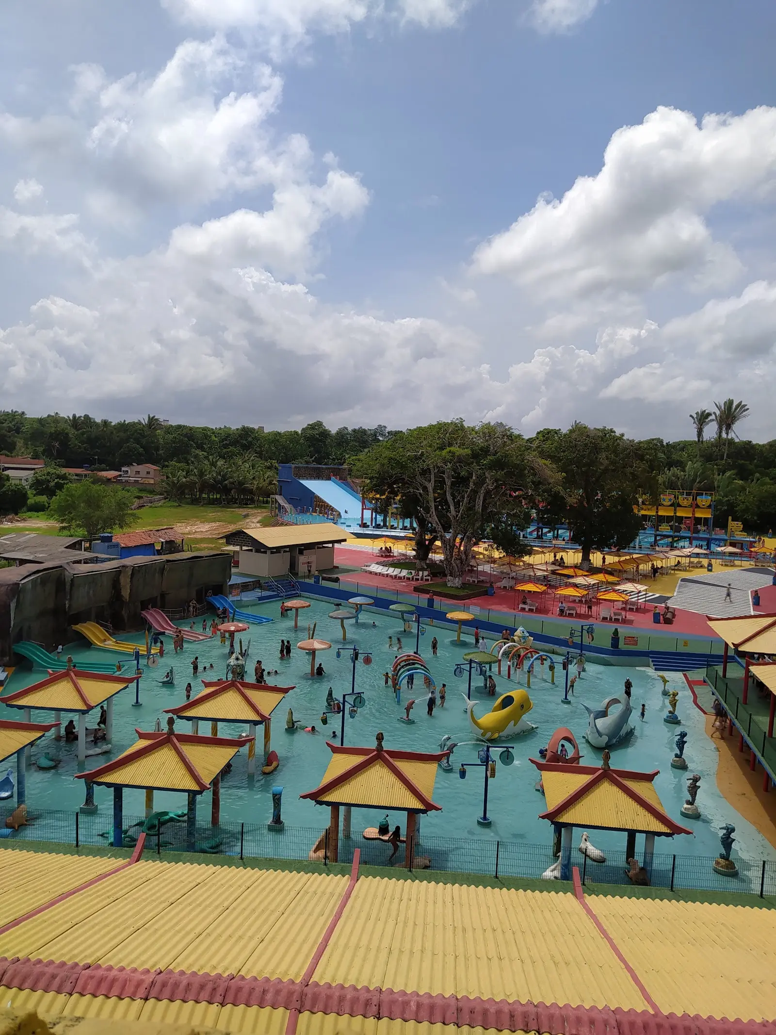 Vista do alto das piscinas do Wang Park, com quiosques de telhado amarelo, escorregadores e guarda-sóis em Paço do Lumiar