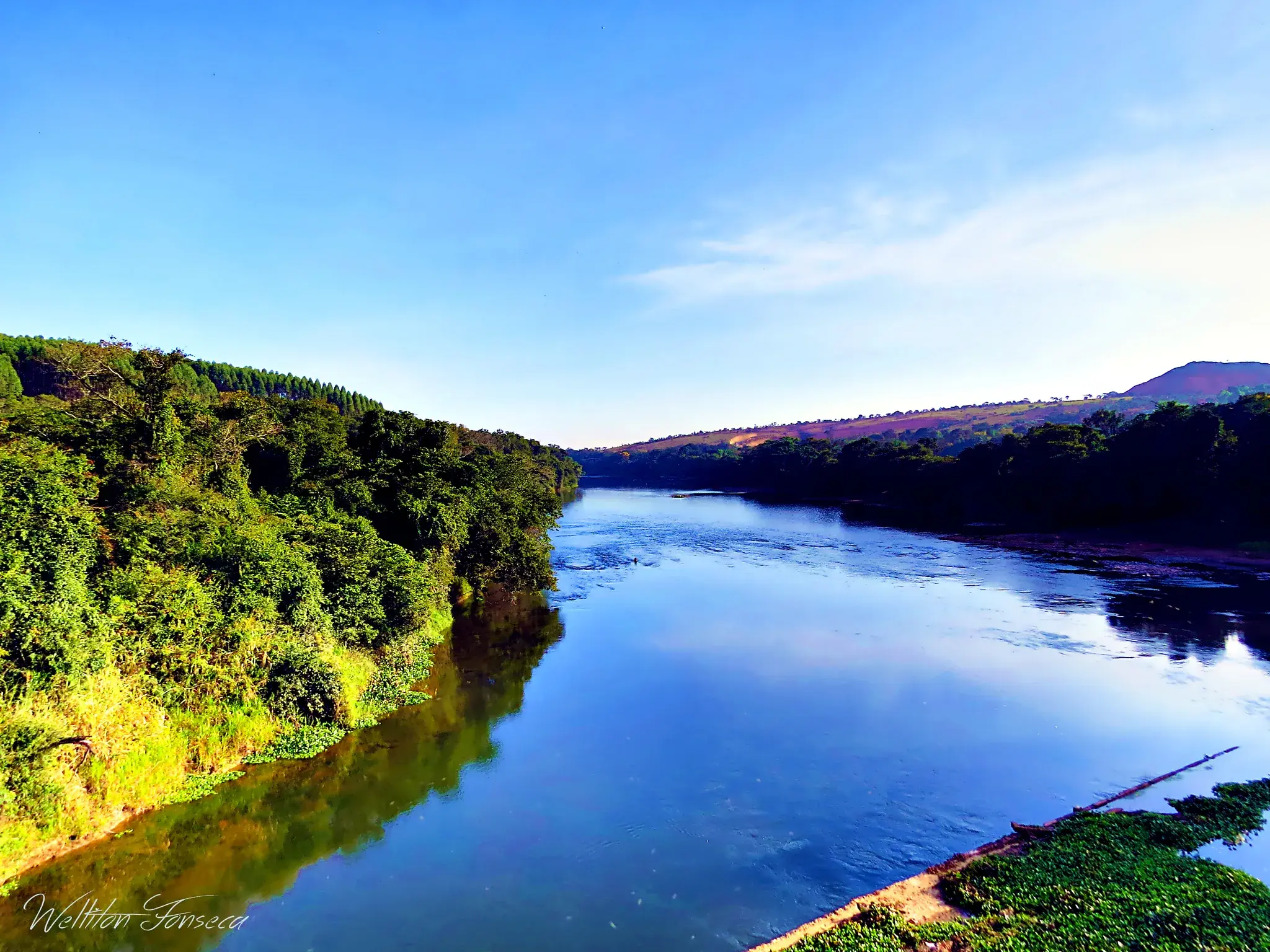 Rio Pará largo e azul visto de uma ponte, com mata na margem e serra ao fundo