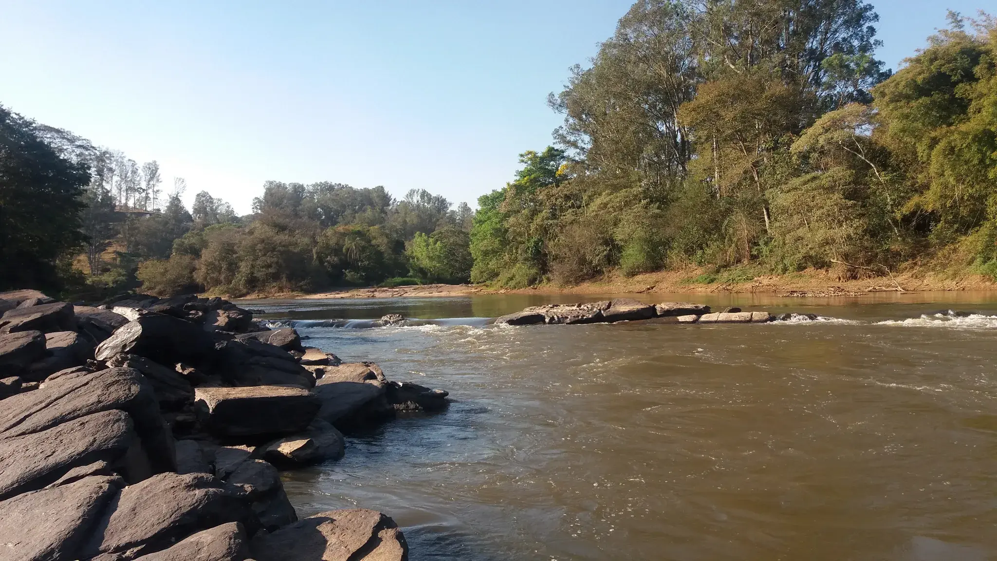 Rio Verde correndo sobre lajes de pedra, com mata e eucaliptos na margem