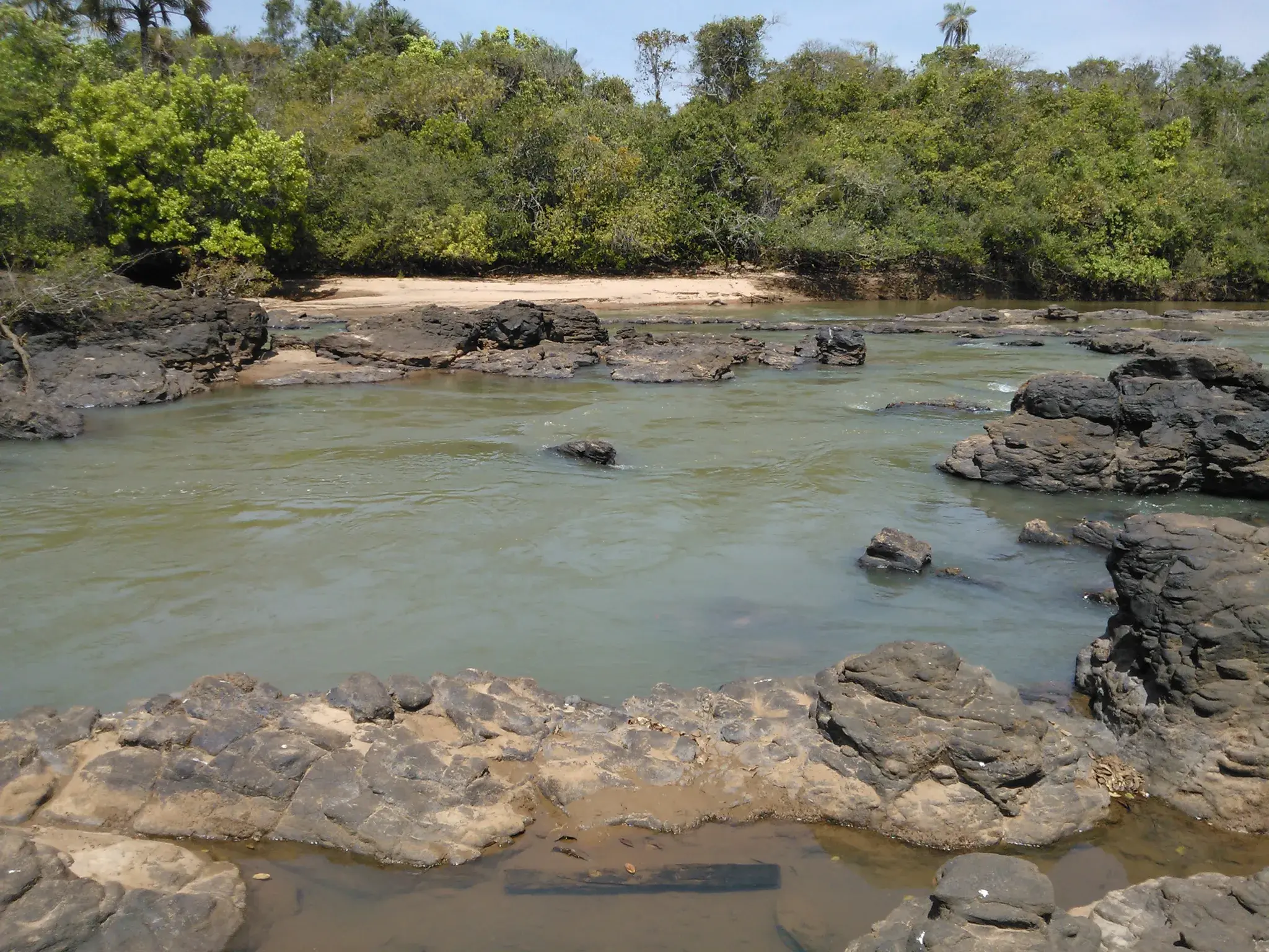Rio da Prata de água clara correndo entre lajes de pedra escura, com prainha e mata ao fundo
