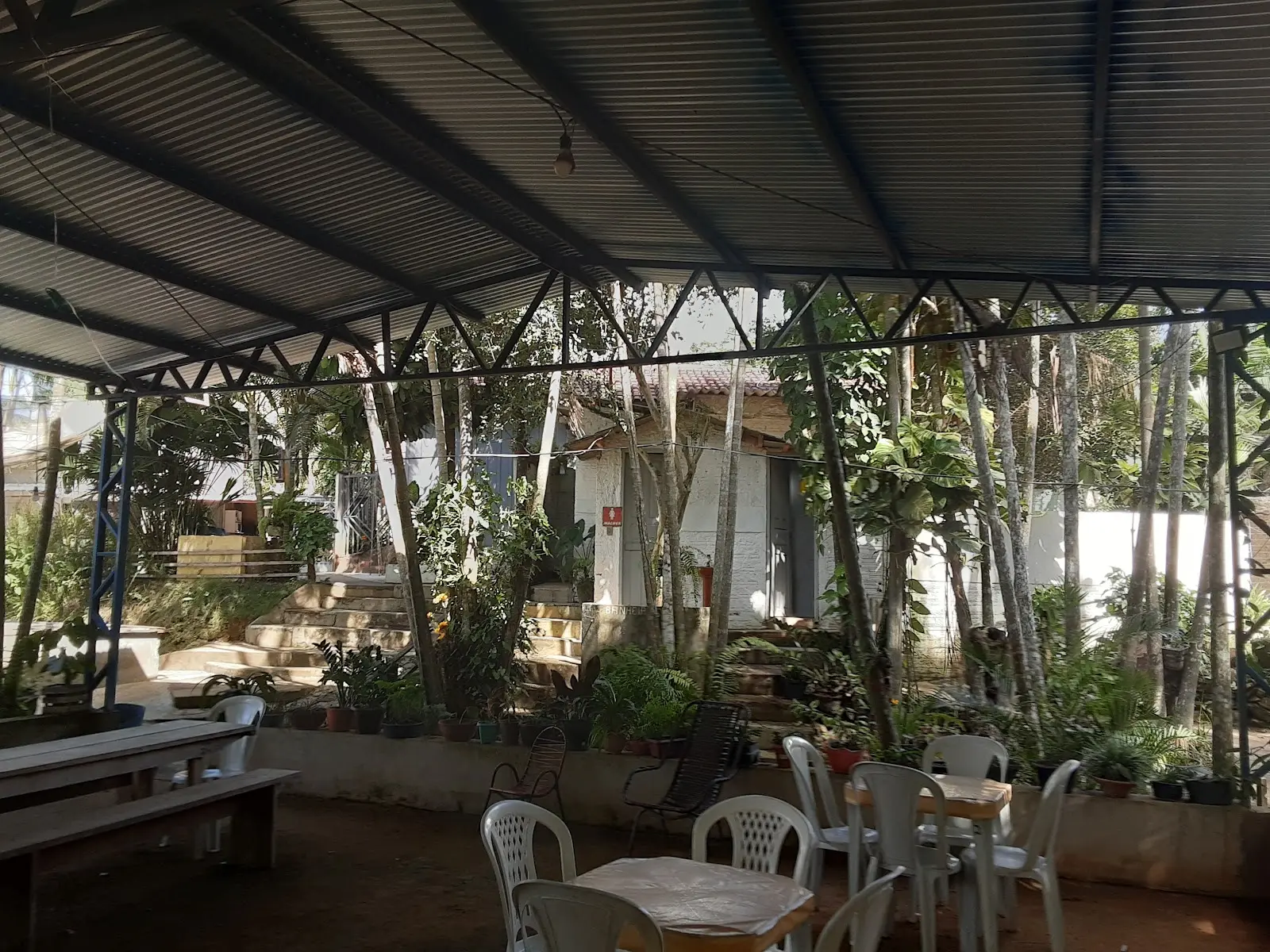Área coberta com mesas e cadeiras de plástico brancas e vasos de plantas no Gauchinho Pesque Pague, em Xinguara