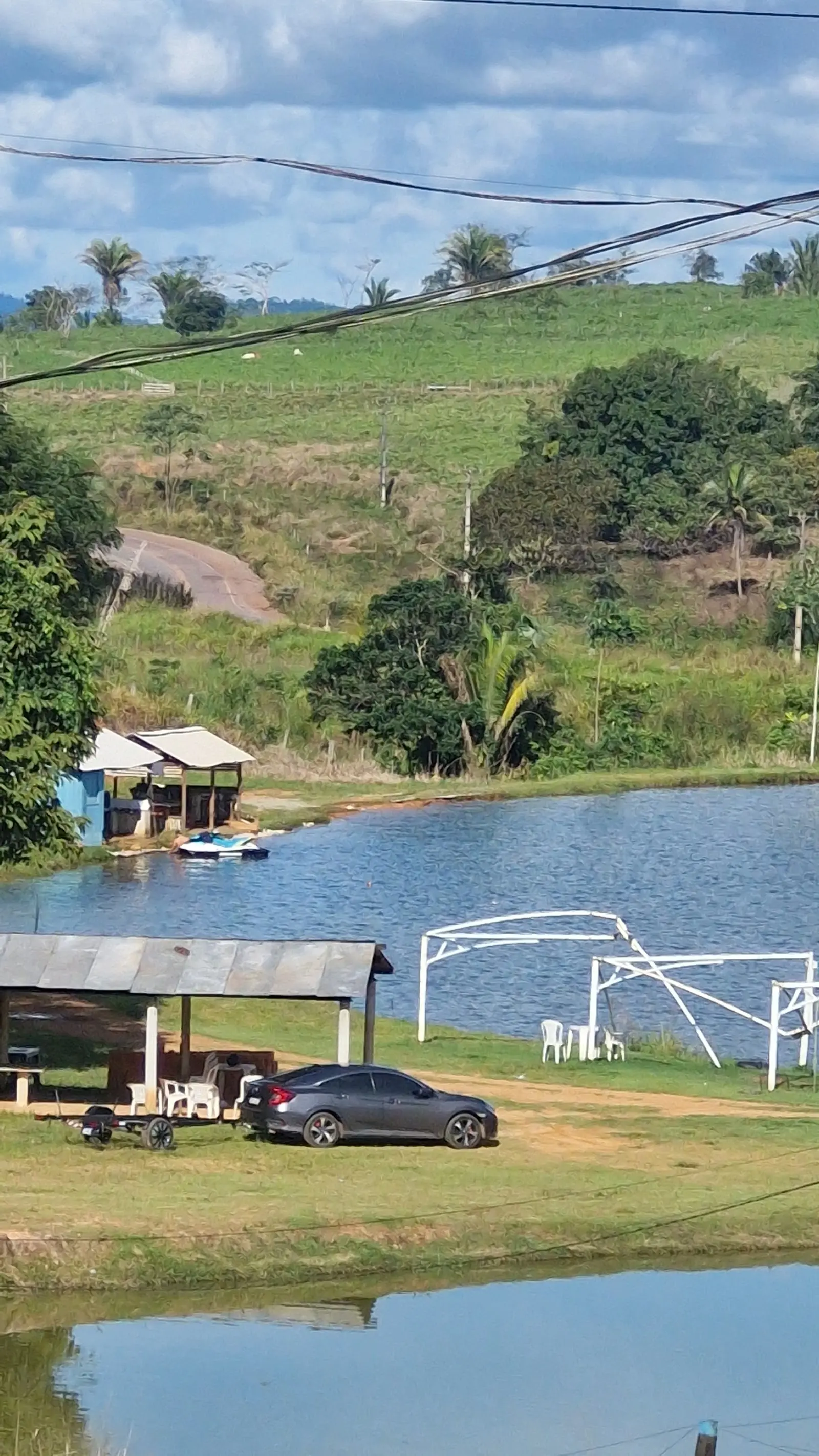 Lago do Pesque Pague do Odair com um jet ski parado na margem, quiosques cobertos e morros de pasto ao fundo