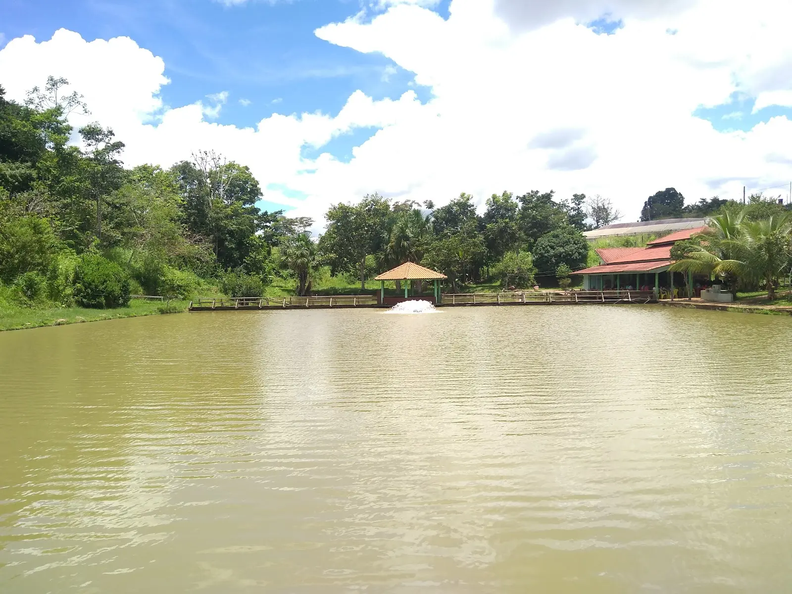 Lago amplo do Pesque Pague Vila Rica, em Colorado do Oeste, com aerador ligado, deck de madeira e quiosque ao fundo