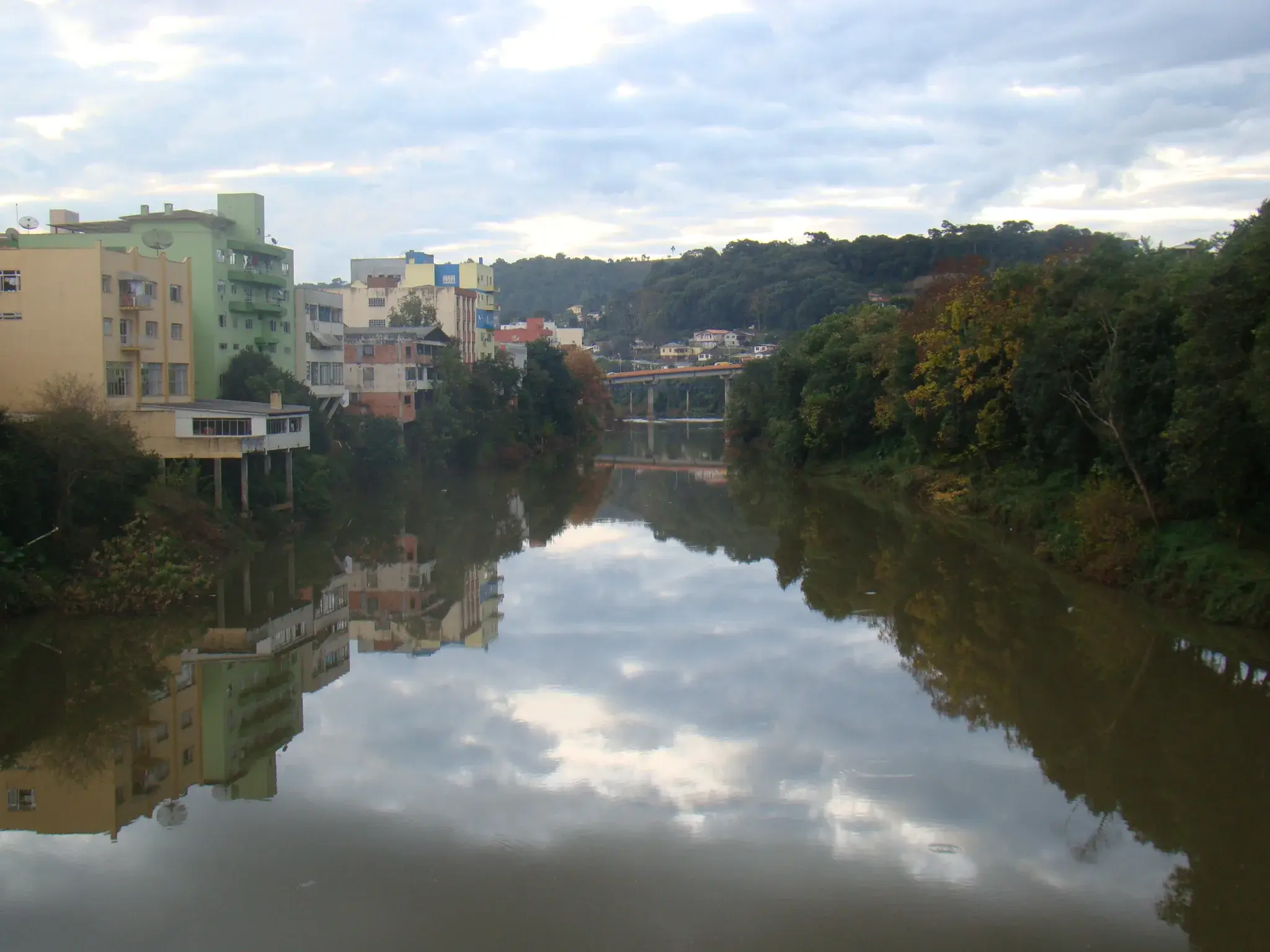 Rio do Peixe calmo atravessando a cidade, com prédios e uma ponte refletidos na água