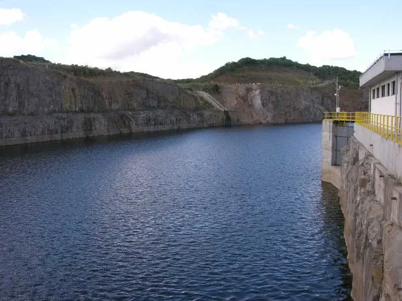 Lago da represa cheio junto à barragem, com paredões de rocha ao fundo