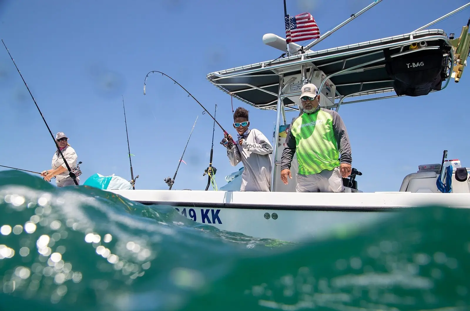 Jovem pescador com a vara envergada logo depois da fisgada, num barco de pesca no mar