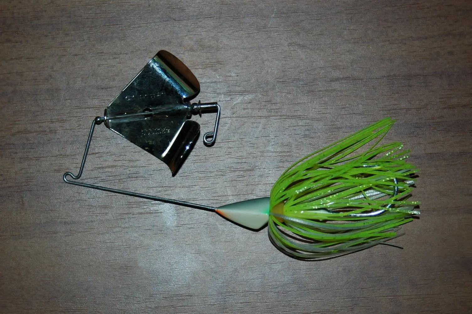 Buzzbait com hélice metálica e saia de silicone verde sobre fundo de madeira
