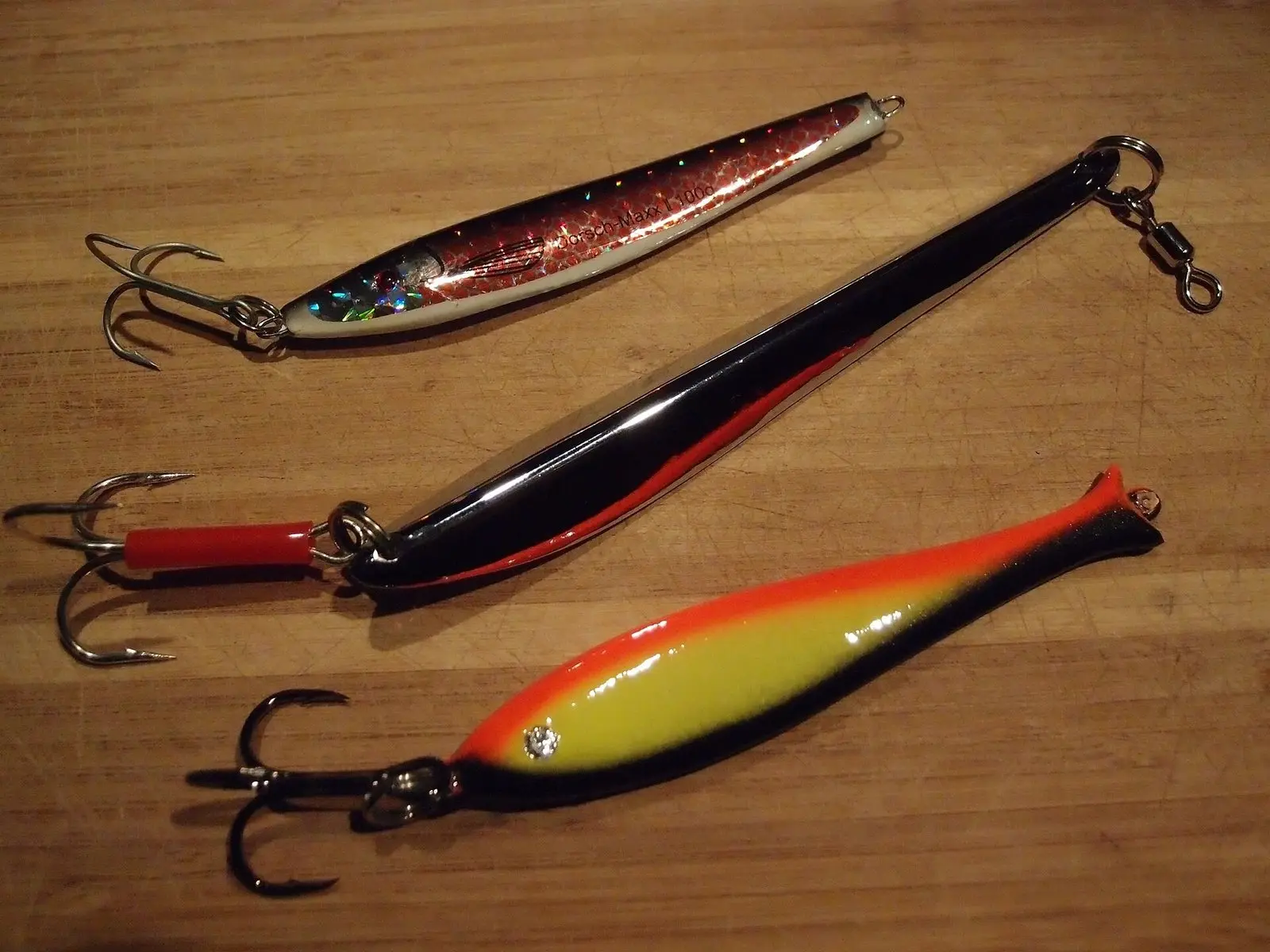 Três jigs metálicos com garatéias sobre uma mesa de madeira