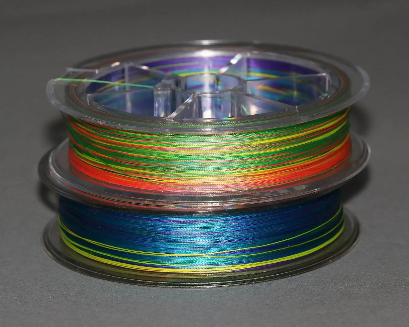 Dois carretéis de linha multifilamento colorida de 8 fios empilhados sobre fundo cinza