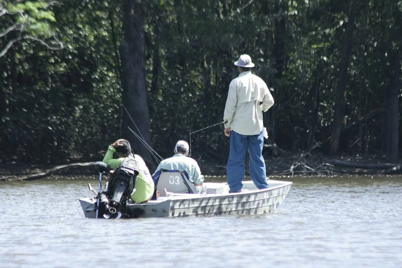 Pescadores num barco de alumínio, um deles em pé arremessando rente à mata alagada na Amazônia