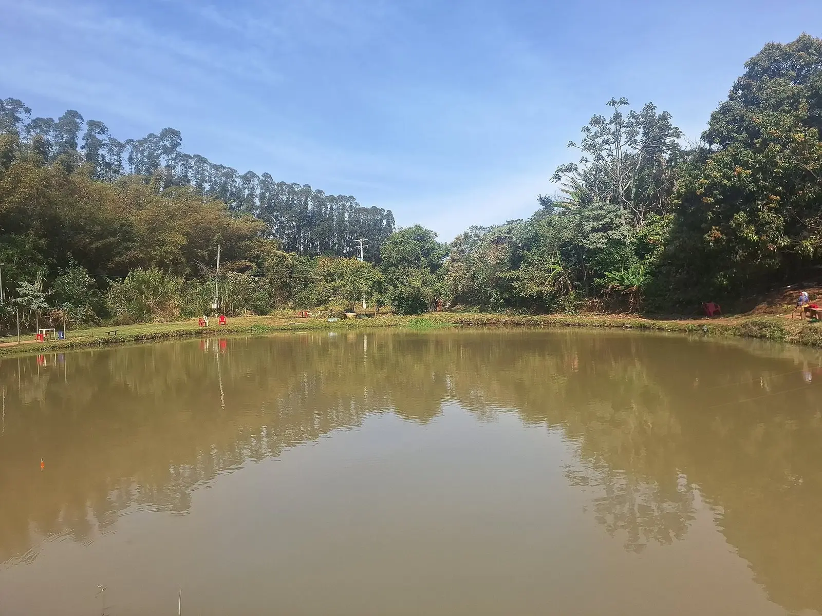 Tanque de pesque-pague com água barrenta, boia laranja e pescadores na margem em Botucatu (SP)