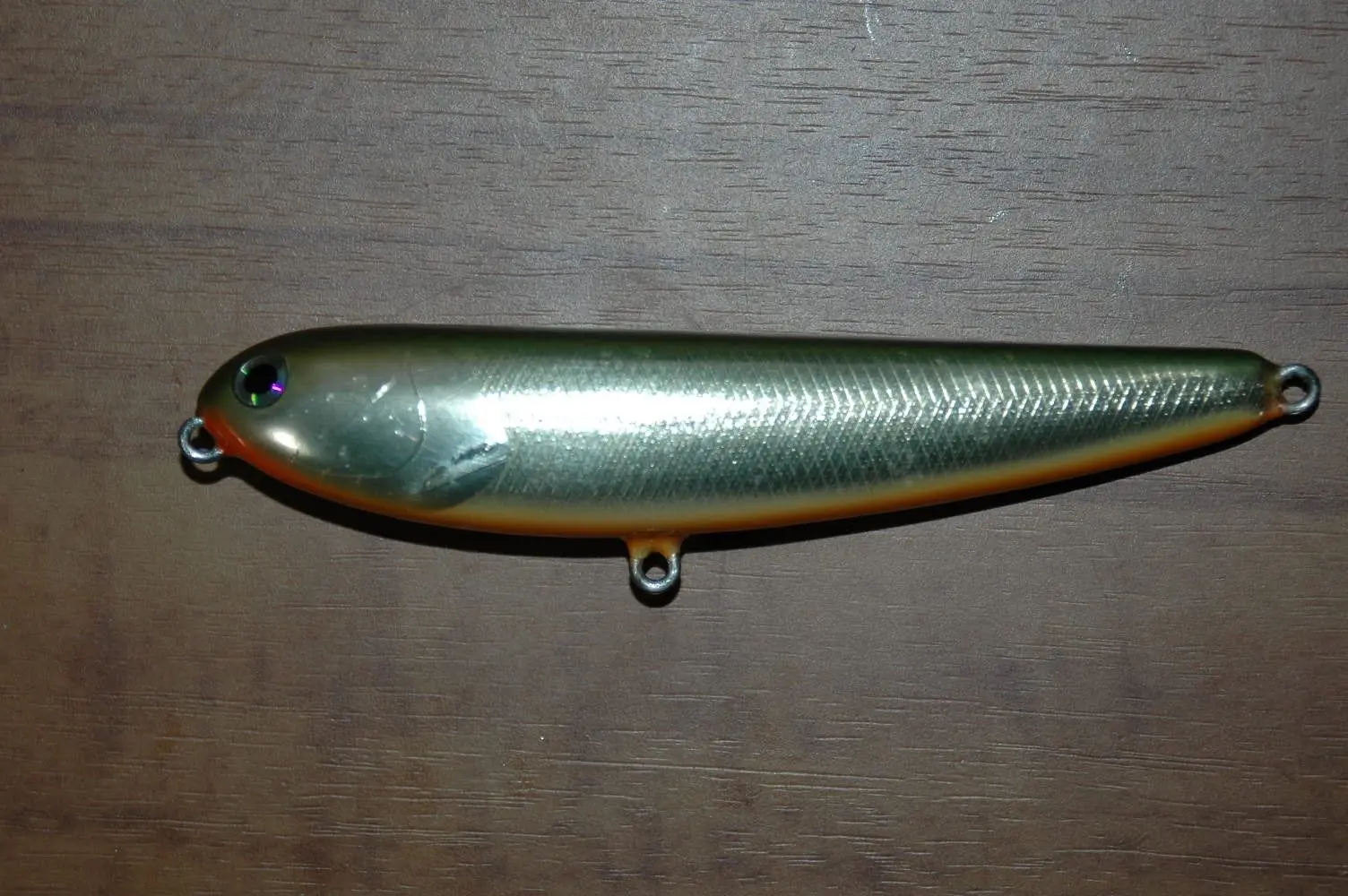 Isca de superfície tipo stick bait, corpo longo e fino, ainda sem as garatéias, sobre madeira