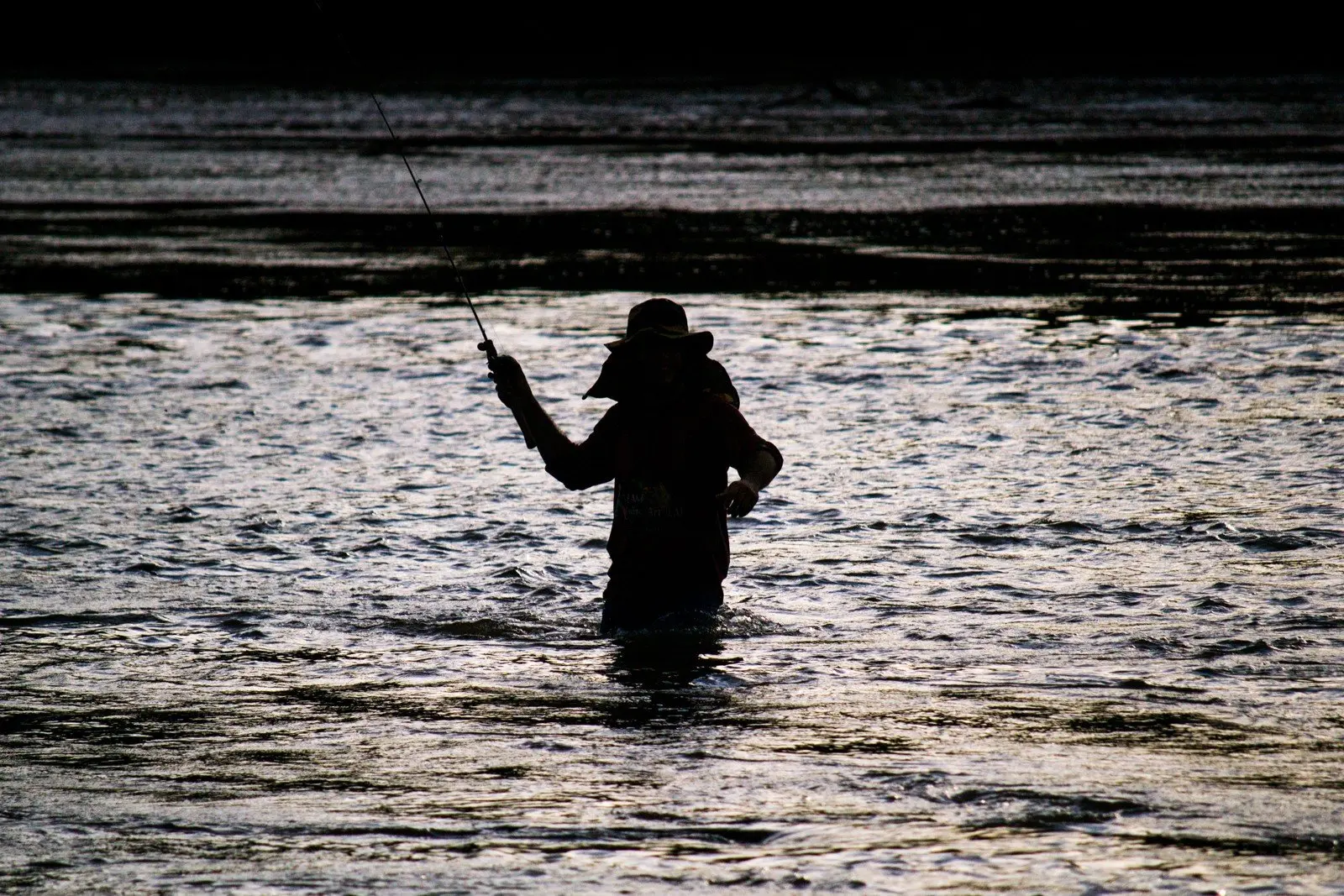 Silhueta de pescador com vara dentro do rio Cuiabá, com a água pela cintura, ao entardecer